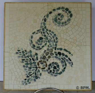 Ceci est une photo de la mosaique de Chantal, en galets et grès cérame représentant un motif végétal à volutes. Ceci est une photo de la mosaique de Chantal, en galets et grès cérame représentant un motif végétal à volutes.