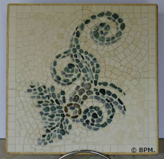 Ceci est une photo de la mosaique de Chantal, en galets et grès cérame représentant un motif végétal à volutes.